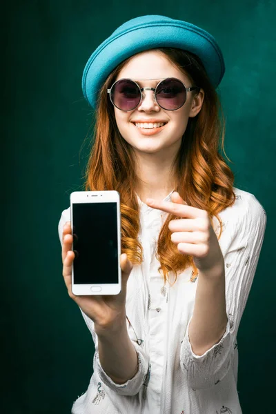 Kafasındaki bir parmak telefonun ekranında gösterilen sevimli bir şapka ile Kızıl saçlı kız