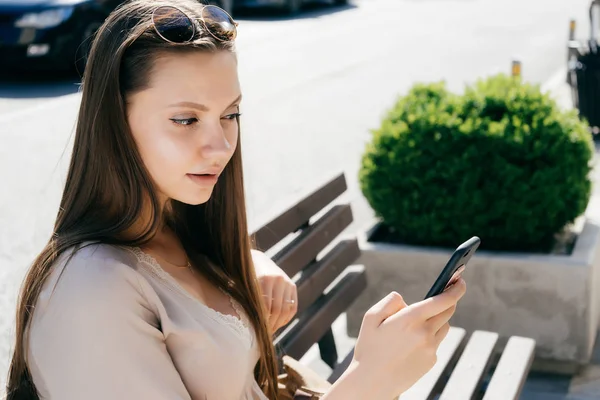 Young modern girl with interest looks at the screen of her smartphone, on the street — Stock Photo, Image