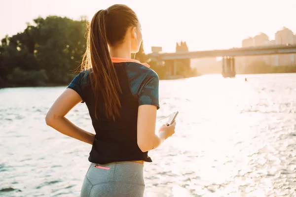 Flickan är engagerade i Sport hörlurar vid floden — Stockfoto