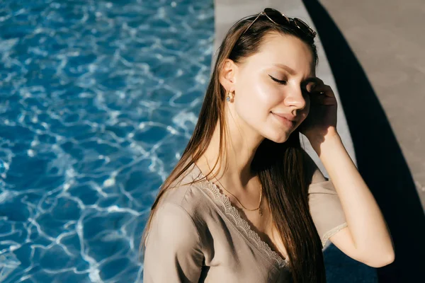 Sorridente ragazza seduta vicino all'acqua blu al sole — Foto Stock