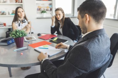 2 hatun ve bir adam ofiste bir masada oturan ve işlerini tartışıyor