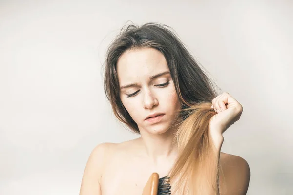 Девушка пытается расчесать свои длинные волосы деревянной расческой — стоковое фото