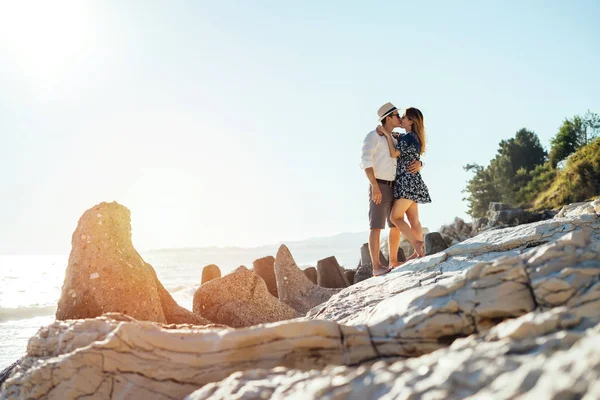 Beautiful young couple kissing on the beach surrounded by rocks — Stock Photo, Image