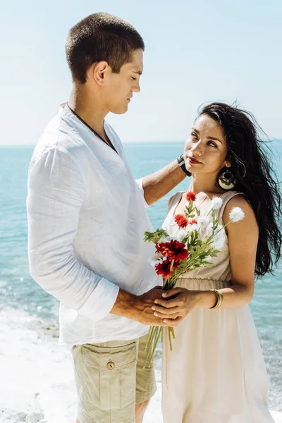 Deux amants se tiennent sur une falaise, un mec donne des fleurs à une fille, romance en vacances — Photo