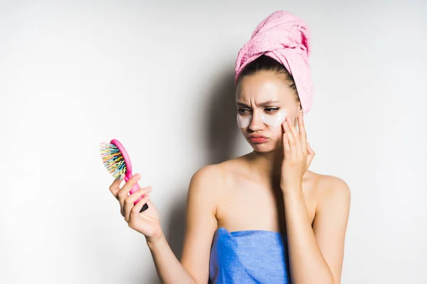 Menina com uma toalha rosa na cabeça olha no espelho e parece triste — Fotografia de Stock