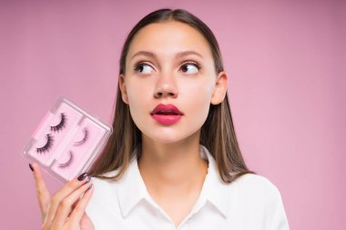 Kız Beyaz gömlekli sahte kirpik elinde tutan ve bir kenara görünüyor