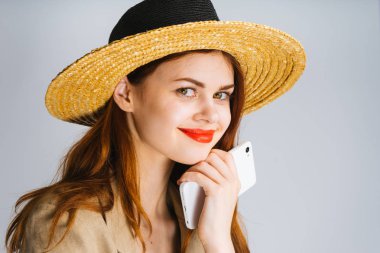 Hasır Şapkalı gülümseyen kız beyaz bir telefon tutarak