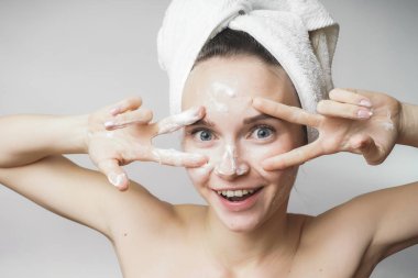 komik kadın mutlu kafasına bir havlu izole beyaz bir arka plan üzerinde köpük ile cildi temizler. Bu barış işareti