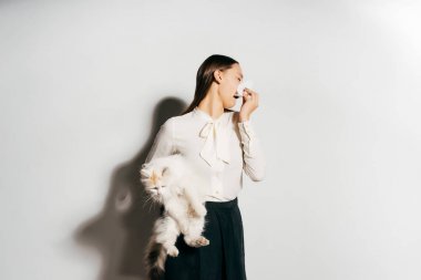 bir kız bir alerji nedeniyle hapşırma ve bir kedi onun kollarında tutar