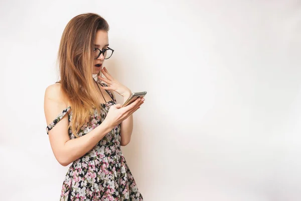 Chica en vestido mira en el teléfono y se ve sorprendido — Foto de Stock