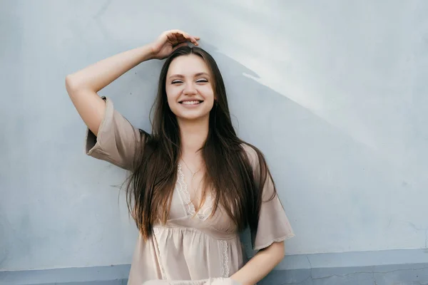 Hermosa chica con el pelo largo sentado en la pared y riendo — Foto de Stock