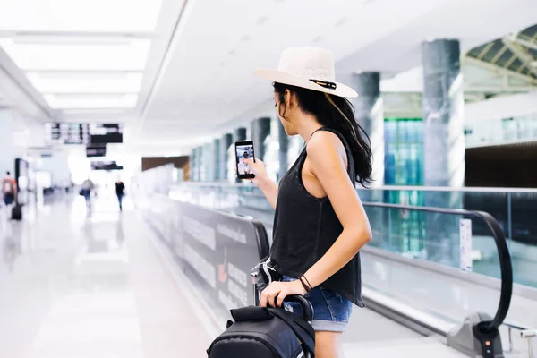 Travel woman using smartphone at airport. Young eastern traveler makes photo with mobile phone app — Stock Photo, Image