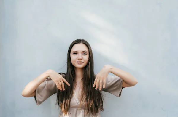Chica con el pelo largo se levanta contra la pared gris y posa — Foto de Stock