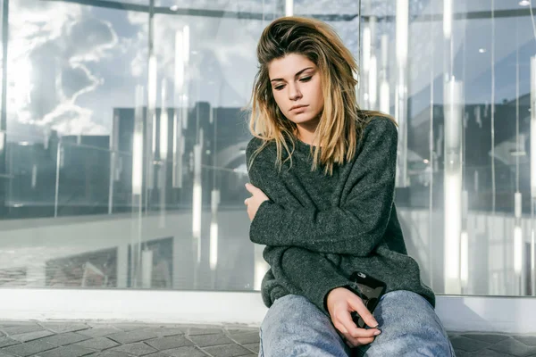 sad girl with thick hair sitting near a glass wall