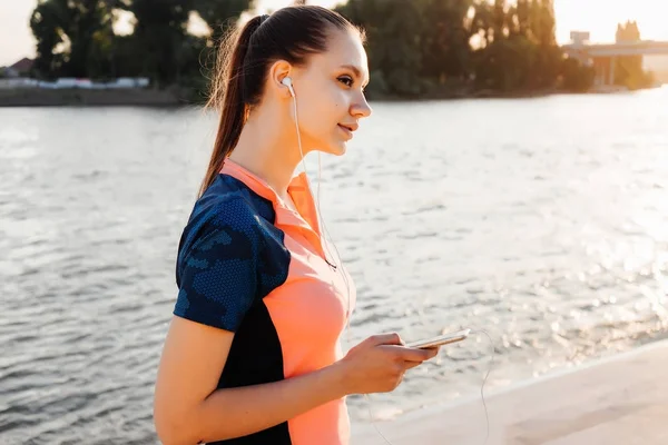 Flicka i sportkläder lyssnar på musik i hörlurar och leende — Stockfoto