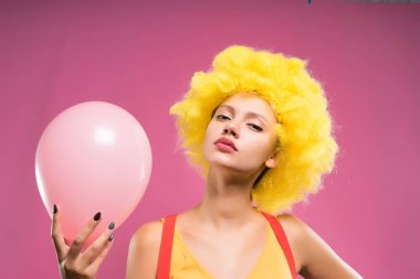 bir kız sarı peruk içinde gururla görünüyor ve bir pembe hava balonu elinde tutan