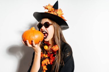 Siyah gözlüklü cadı elbiseli bir kız bir kabak ısırmaya çalışır