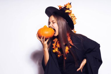 Cadı elbiseli bir kız küçük kabak bir parça kapalı ısırmaya çalışır