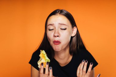 Sinirli bir kız ona burger turuncu bir arka plan üzerinde dışında bir ısırık alır