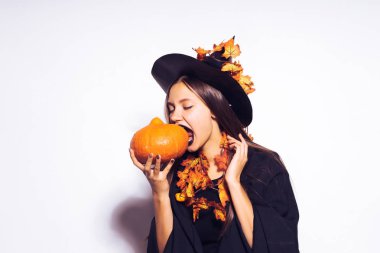 Beyaz bir arka plan üzerinde küçük bir kabak bir parça ısırmaya çalışıyor cadı elbiseli kız