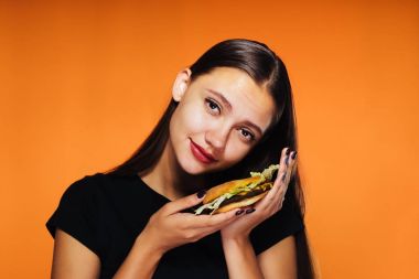 Hamburger turuncu bir arka plan üzerinde tutarak gülümseyen kız