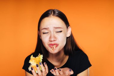 hayal kırıklığına uğramış kız turuncu bir arka plan üzerinde onun elinde bir hamburger yiyor