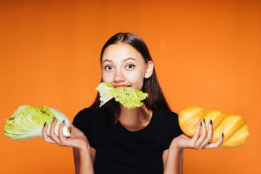 turuncu bir arka plan üzerinde bir kız onun elleri marul yaprakları ve bir parça ekmek tutan