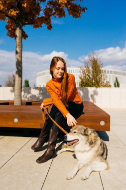 Onu köpek ile bir bankta oturan gülümseyen kız