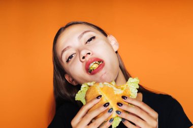 Kız onun elinde turuncu bir arka plan üzerinde bir hamburger yiyor