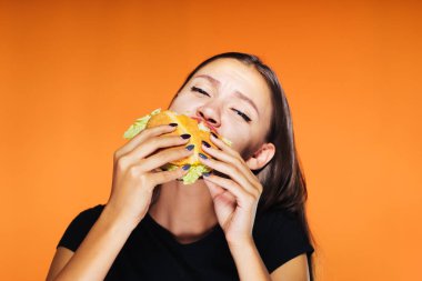 Kız onun elinde hamburger yeme turuncu bir arka plan üzerinde