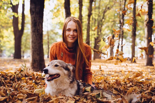 Mädchen im orangefarbenen Pullover streichelt ihren Hund im Herbstpark — Stockfoto