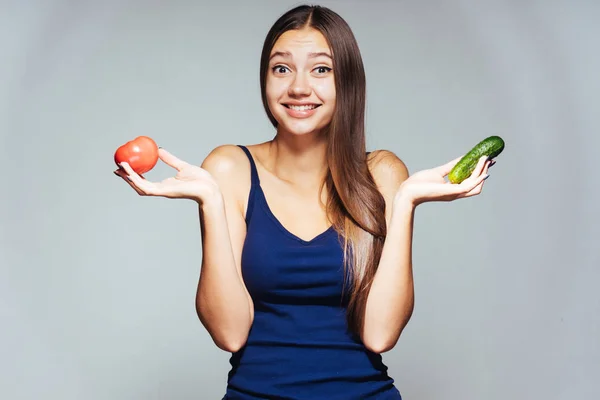Usmívající se dívka stojící na bílém pozadí, držící v rukou rajče a okurka — Stock fotografie