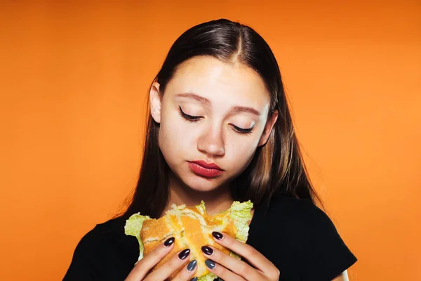 Upset girl holding a big burger on an orange background — Stock Photo, Image
