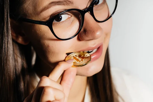 在试图啃她的牙齿与一枚硬币的白色背景上的眼镜的女孩 — 图库照片