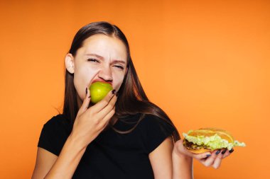 bir kız başka bir burger tutarak onun elinde bir elma yiyor