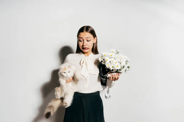 Überraschtes Mädchen mit einer Katze und einem Blumenstrauß in der Hand — Stockfoto