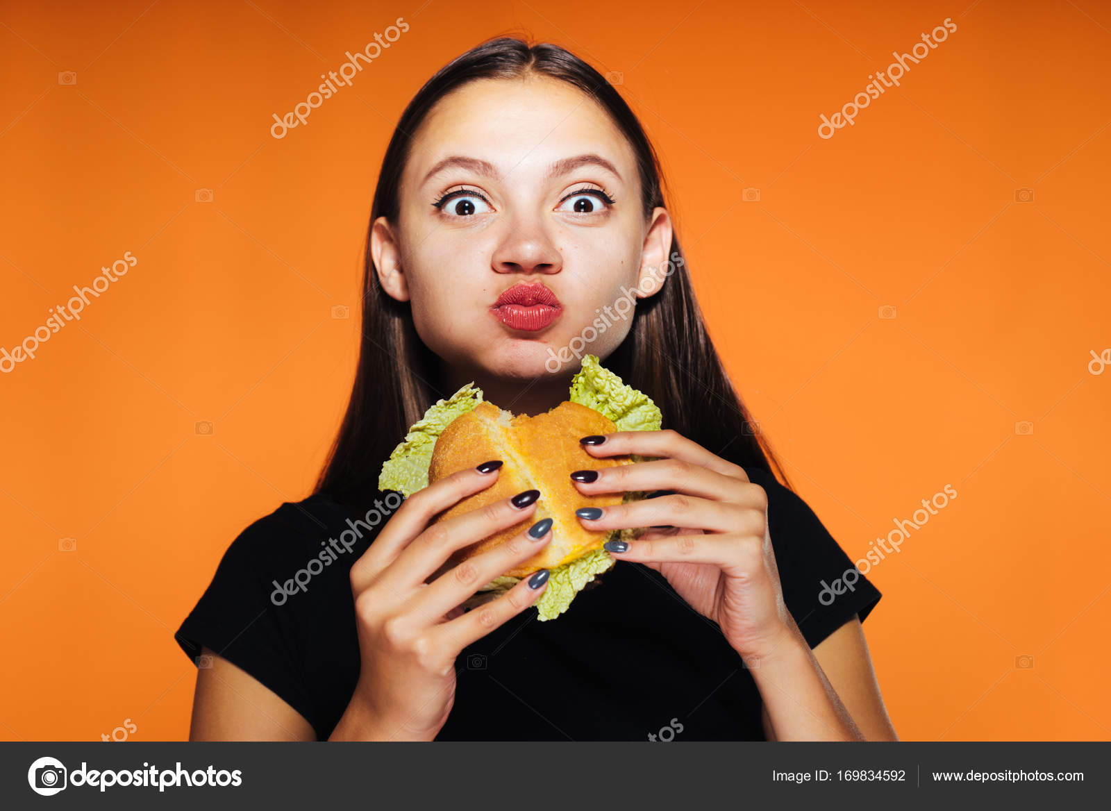Beautiful hungry girl greedily eats up her burger and looks at the
