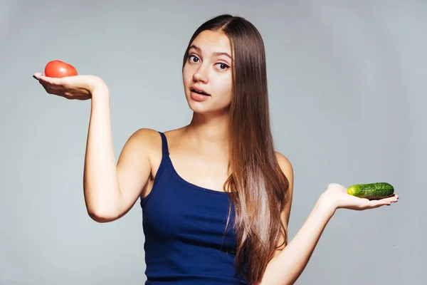 Förvånad tjej ser på kameran och innehar en tomat och gurka, grönsaker, kost — Stockfoto