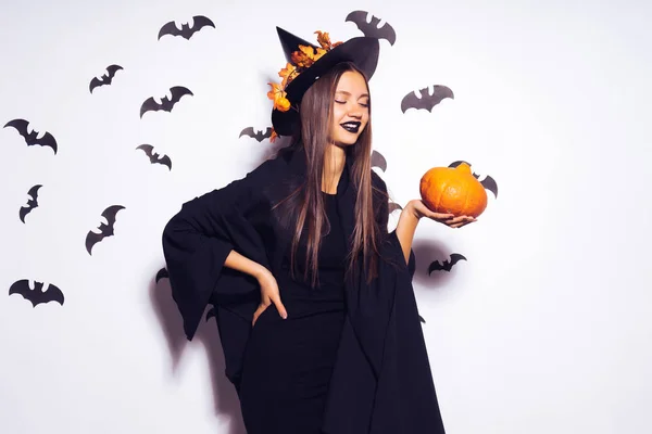 Ampia Halloween party art design Strega di Halloween con una zucca intagliata e in un terribile cappello nero sorride. Sullo sfondo di un mucchio di pipistrelli . — Foto Stock