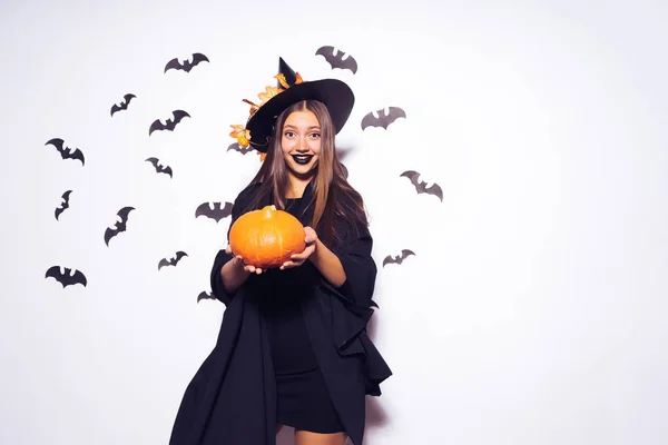 Breed Halloween party kunst design Halloween heks met een gesneden pompoen en in een zwarte verschrikkelijke hoed glimlacht. Tegen de achtergrond van een bos van vleermuizen. — Stockfoto