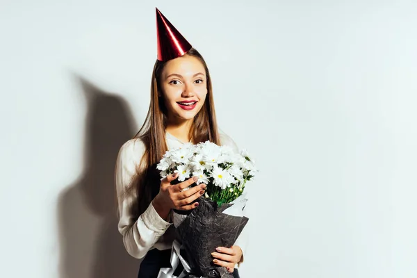 Tener un hermoso cumpleaños de chica. La señora está de pie con un ramo de manzanillas y una gorra roja festiva. Feliz cumpleaños. — Foto de Stock