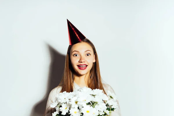 Beautiful happy girl with a chic bouquet of romomiles, isolated, birthday, holiday, joy, festive cap — стоковое фото