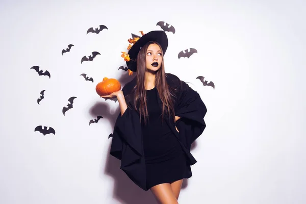 De heks meisje was gonna een partij in de Halloween-outfit en houden van een pompoen, een zwarte hoed, vleermuizen in de achtergrond — Stockfoto