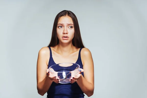 Triste, chica hambrienta está sosteniendo un tazón vacío áspero en sus manos y mira hacia los lados . — Foto de Stock