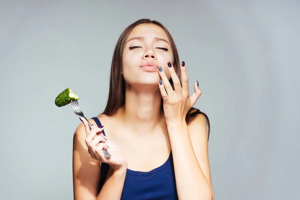 Une fille en maillot bleu mange un concombre et se frotte la bouche avec son doigt, délicieux aliments sains — Photo