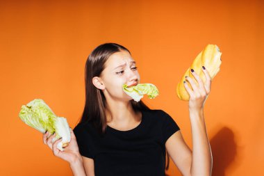Kız bir lahana ve bir somun onun elinde tutar. Lahana, turuncu zemin üzerine izole çiğneme kız