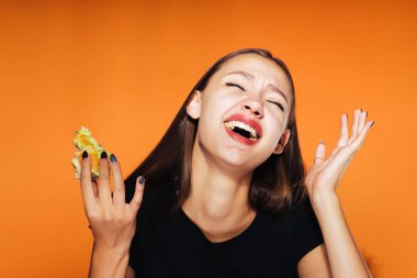 Aç kız onun hamburger yiyor. Kız gözleri kapalı gülüyor. Çok lezzetli yemekler, turuncu bir arka plan üzerinde izole