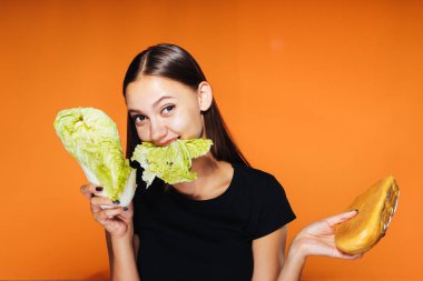 Kız bir lahana ve bir somun onun elinde tutar. Lahana, turuncu zemin üzerine izole çiğneme kız
