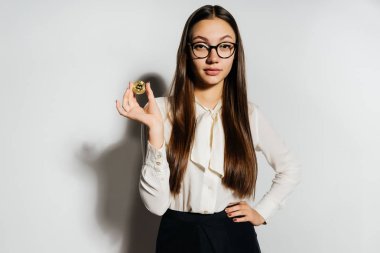 Güzel bir kız gözlük ve beyaz bir bluz altın sikke onun elinde tutan ve kameraya doğru görünüyor. Elektronik para, bitcoins, kripto para birimi.