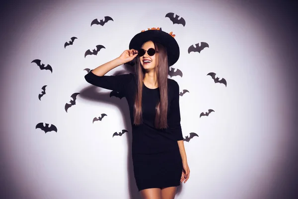 긴 머리와 안경 할로윈 소녀입니다. 할로윈 여자 블랙 할로윈 드레스와 박쥐의 무리의 끔찍한 배경에 오렌지 잎 모자를 쓰고. — 스톡 사진